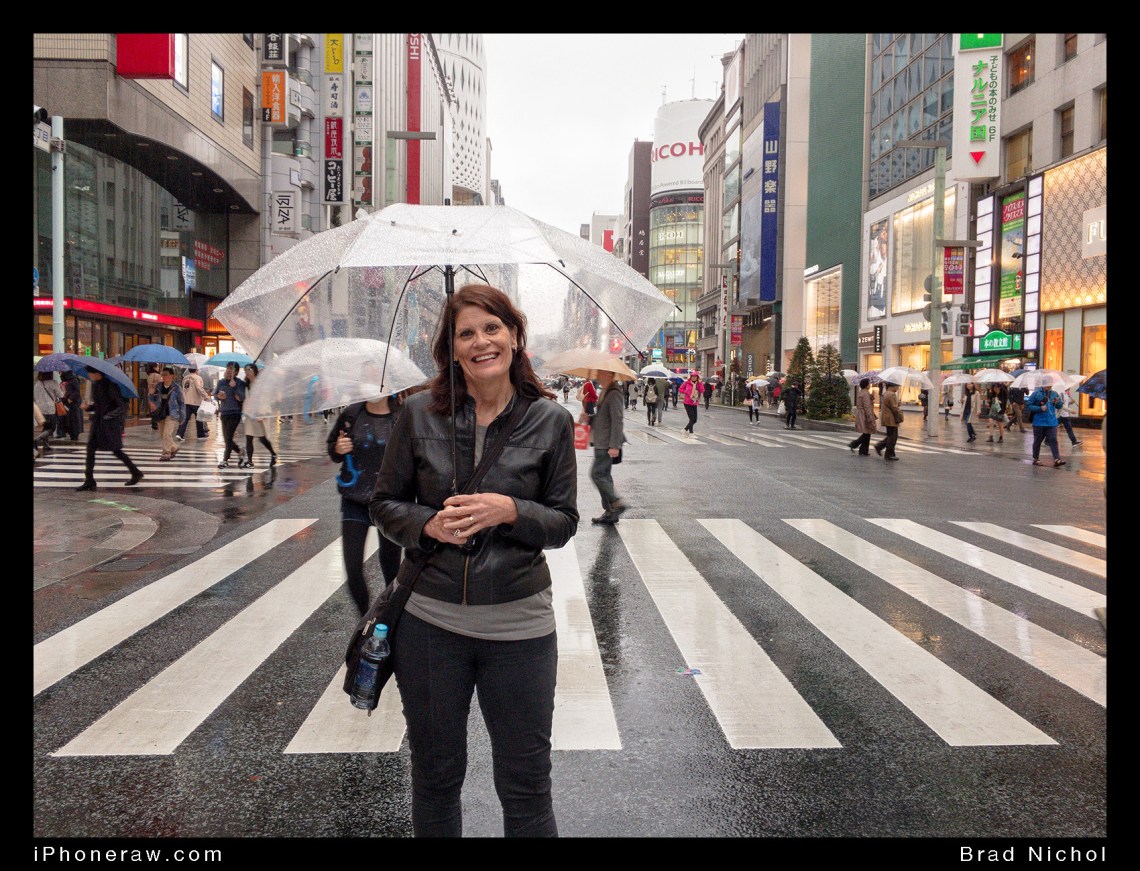Lady standing in street under umbrella, Ginza, Japan, during Typhoon season, roads clear of cars.